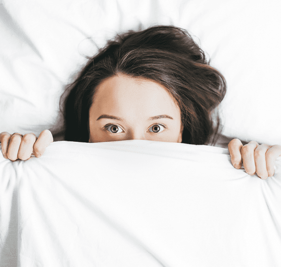 Manage your nerves better, woman hiding under bed sheets. Credit Alexandra Gorn